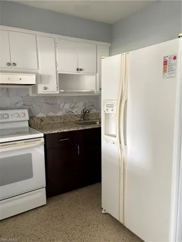 Dual tone kitchen with white appliances, tasteful backsplash, range hood, dark speckled floor, and dual tone cabinetry
