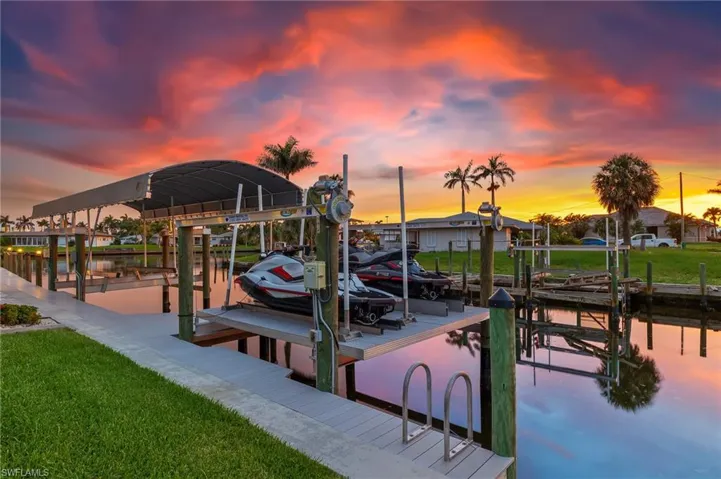Dock featuring boat lift, a water view, and a yard