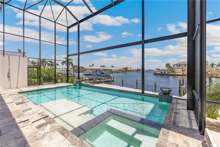 View of pool and spa featuring a pool with connected hot tub, boat lift, a boat dock, a water view, and a lanai