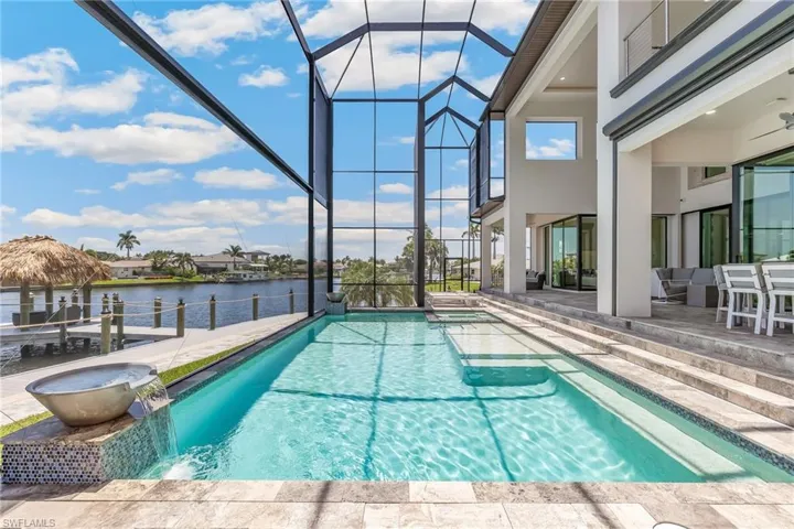 View of swimming pool with a patio, a pool with connected hot tub, glass enclosure, and a water view