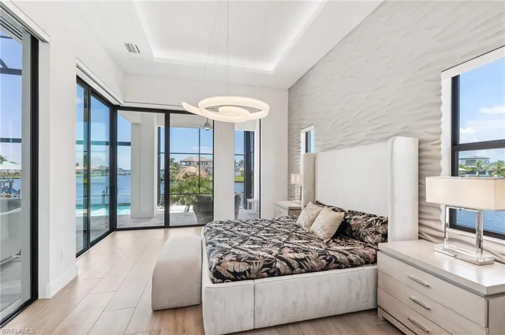 Bedroom featuring a water view, multiple windows, a raised ceiling, and access to exterior