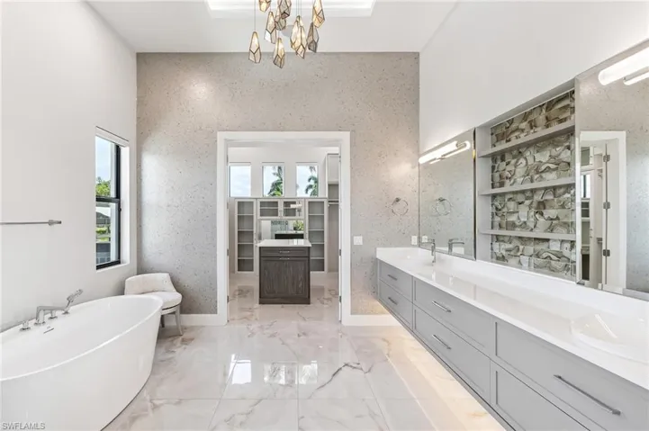 Full bathroom featuring healthy amount of natural light, double vanity, a freestanding bath, and a chandelier