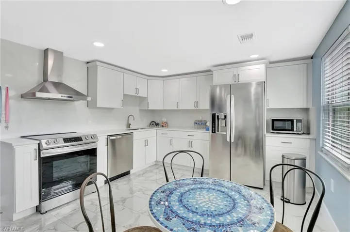 Kitchen featuring stainless steel appliances, light marble finish flooring, white cabinetry, and recessed lighting