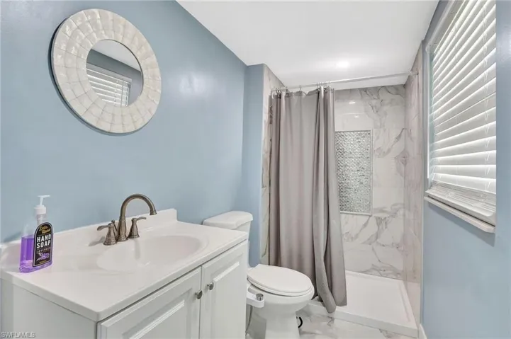 Bathroom with vanity, a marble finish shower, and light marble finish flooring