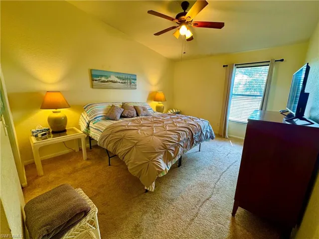 Carpeted bedroom with lofted ceiling, baseboards, and a ceiling fan