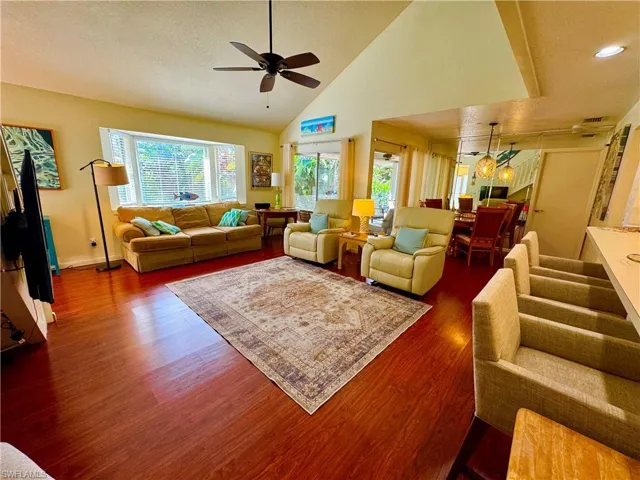 Living room featuring a textured ceiling, high vaulted ceiling, ceiling fan, dark wood-style flooring, and baseboards