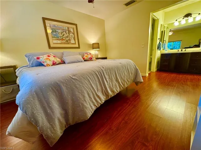Bedroom with baseboards, wood finished floors, visible vents, and connected bathroom