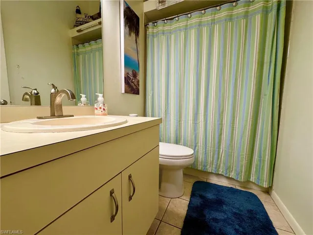 Full bath featuring baseboards, toilet, a shower with curtain, tile patterned flooring, and vanity