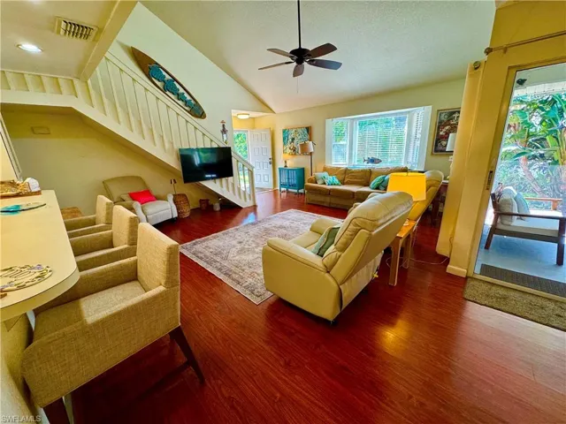 Living area with visible vents, ceiling fan, stairway, wood finished floors, and vaulted ceiling