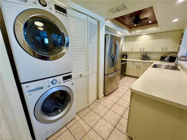 Laundry room featuring stacked washer and clothes dryer, visible vents, a ceiling fan, light tile patterned flooring, and a sink