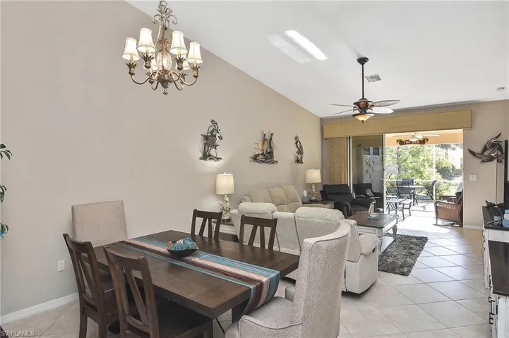 Tiled dining room with vaulted ceiling and ceiling fan with notable chandelier