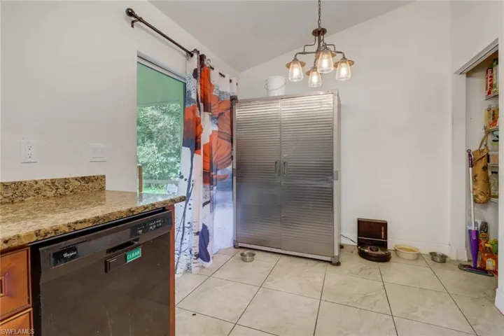 Kitchen featuring pendant lighting, an inviting chandelier, lofted ceiling, black dishwasher, and light tile patterned floors