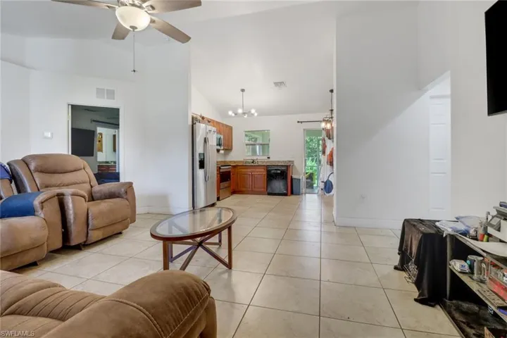 Tiled living room with high vaulted ceiling and ceiling fan with notable chandelier