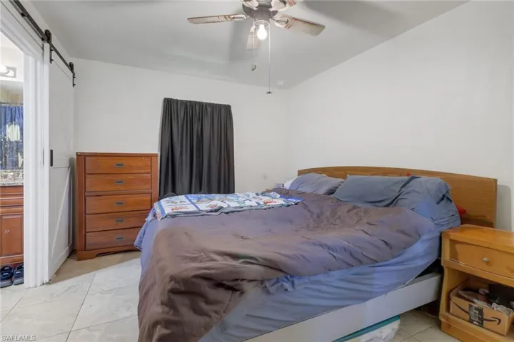 Bedroom featuring ceiling fan, light tile patterned flooring, and a barn door