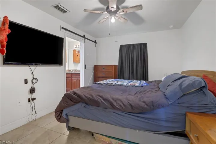 Tiled bedroom featuring connected bathroom, a barn door, and ceiling fan