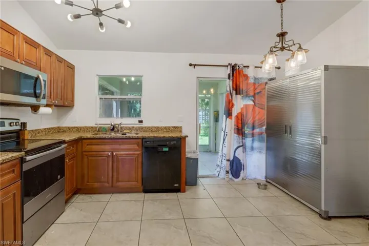 Kitchen with a notable chandelier, appliances with stainless steel finishes, lofted ceiling, light stone countertops, and light tile patterned floors
