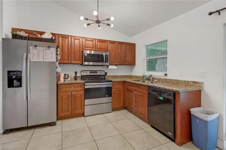 Kitchen with lofted ceiling, light tile patterned floors, appliances with stainless steel finishes, light stone countertops, and an inviting chandelier