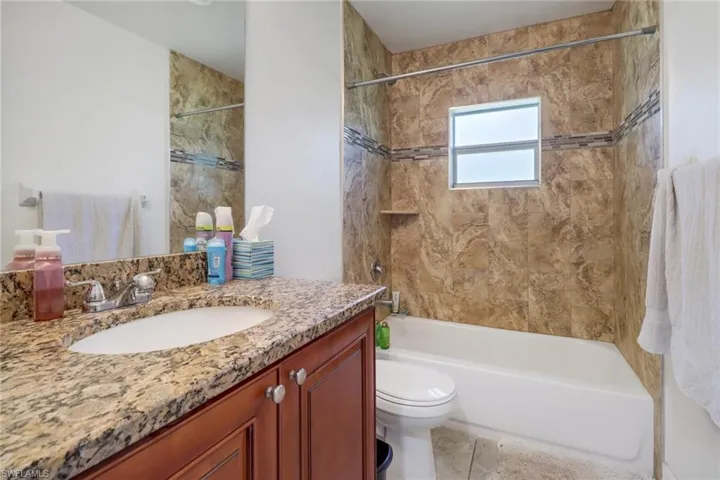 Full bathroom with vanity, tiled shower / bath combo, toilet, and tile patterned flooring