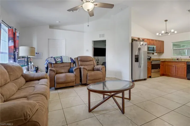 Living room with light tile patterned flooring, sink, ceiling fan with notable chandelier, and high vaulted ceiling
