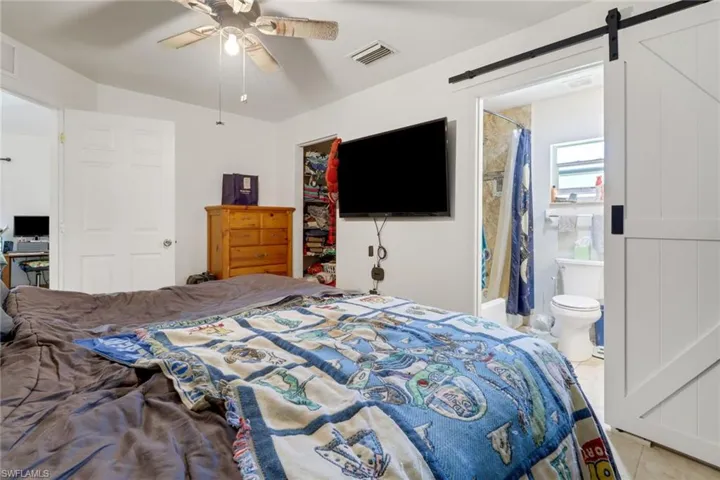 Bedroom featuring ceiling fan, a barn door, ensuite bathroom, and light tile patterned floors