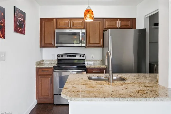 Kitchen featuring rich wood cabinetry, stainless steel appliances, speckled stone countertops, and a built-in sink with a gooseneck faucet