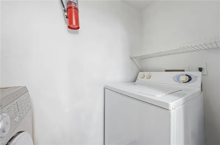 Dedicated laundry area featuring a white top-load washing machine and a wall-mounted wire shelf