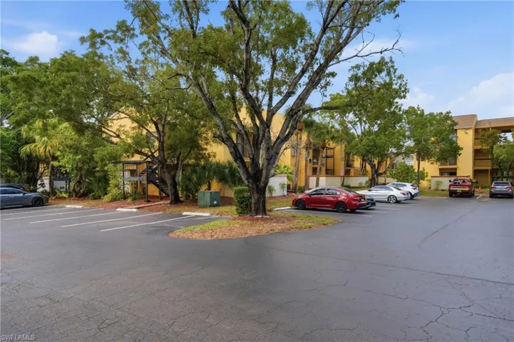 Paved parking lot with marked spaces, surrounded by mature trees and landscaping