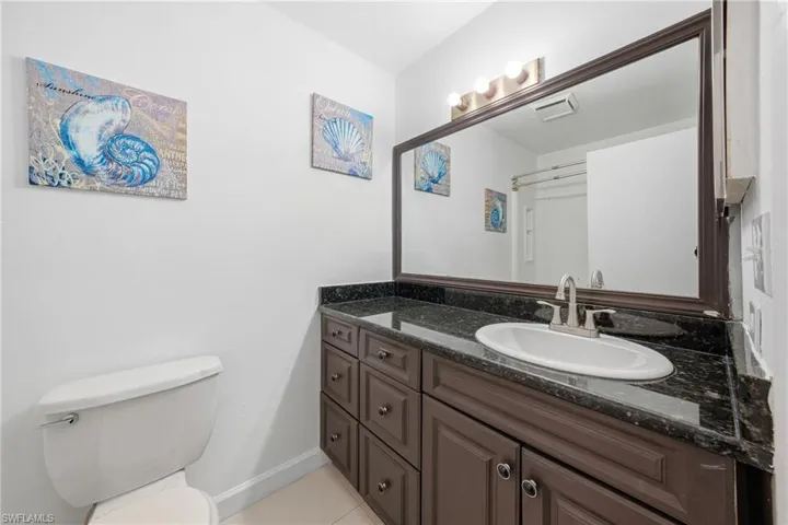 Vanity featuring a dark granite countertop with an undermount sink, a large framed mirror, and a multi-bulb light fixture