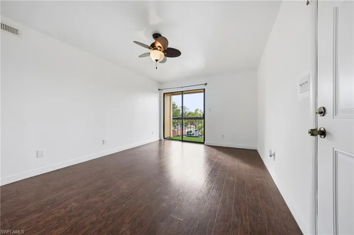 Spacious room featuring wood-finish flooring, white walls, and a ceiling fan with integrated lighting
