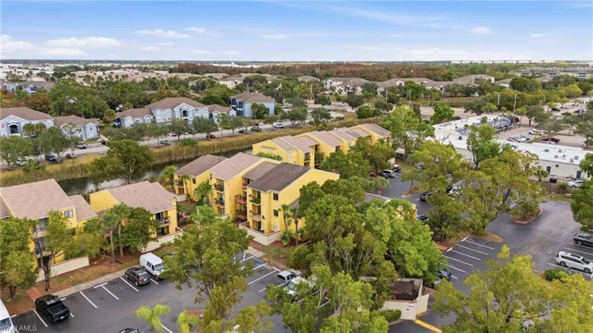 Aerial perspective showcasing multi-story residential buildings with tan exteriors and brown roofs, surrounded by mature trees