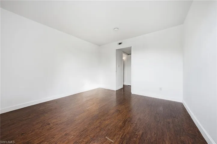 Spacious interior room featuring dark wood-finish flooring, white baseboards, and neutral white wall paint