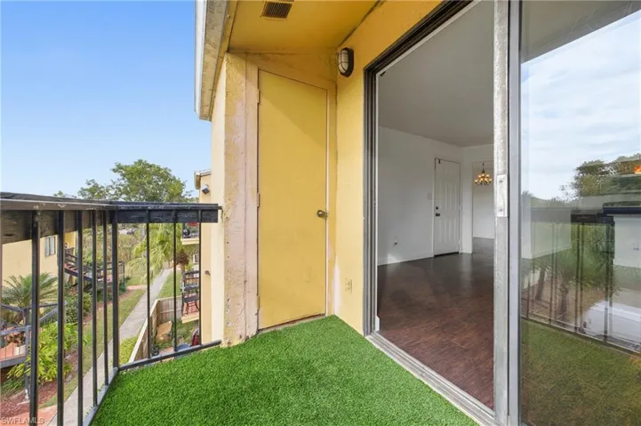 Balcony featuring artificial turf flooring, a black metal railing, and a sliding glass door entry to the interior with wood-finish flooring