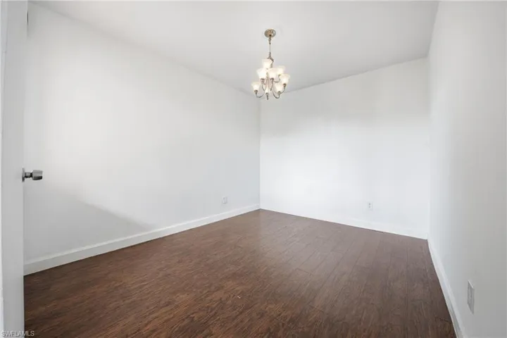 Room with wood-finish flooring, white walls, and a multi-bulb chandelier