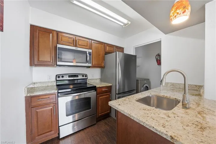 Kitchen featuring granite countertops, stainless steel appliances, wood-finish flooring, and ample cabinetry