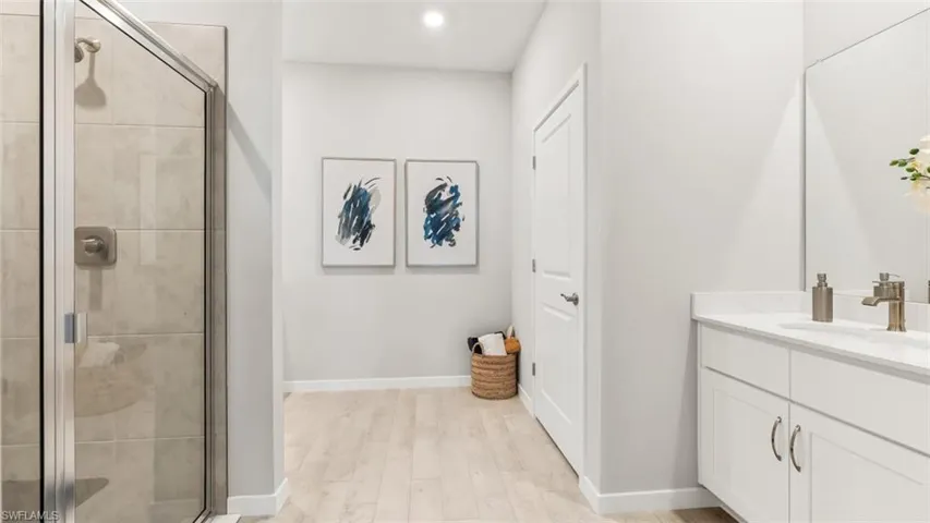 Bathroom featuring a glass-enclosed shower with tiled walls, a vanity with dual sinks, a stone-finish countertop, and light wood-finish flooring