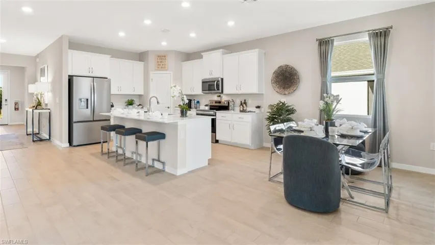 Open-concept kitchen and dining area featuring light wood-finish flooring, white cabinetry, a central island with integrated seating, stainless steel appliances, and recessed lighting