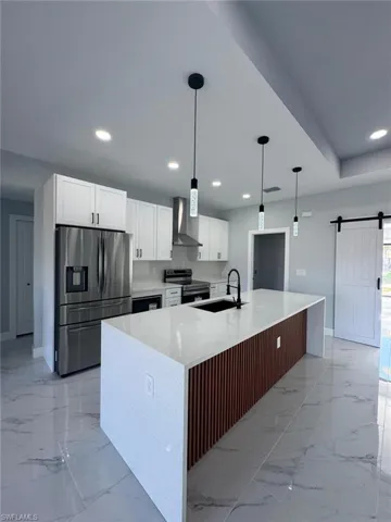 Kitchen featuring appliances with stainless steel finishes, sink, a kitchen island with sink, a barn door, and wall chimney range hood