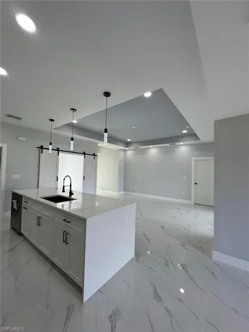 Kitchen with sink, an island with sink, white cabinets, decorative light fixtures, and a barn door