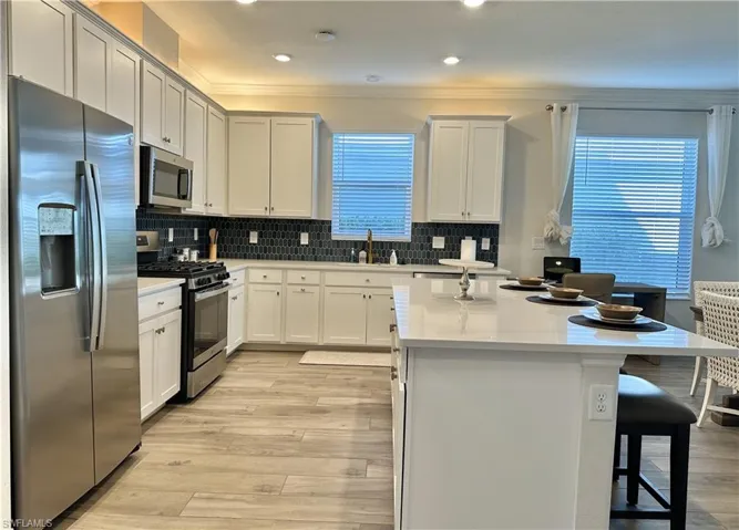 Kitchen with stainless steel appliances, a kitchen breakfast bar, backsplash, a center island, and light wood-style flooring