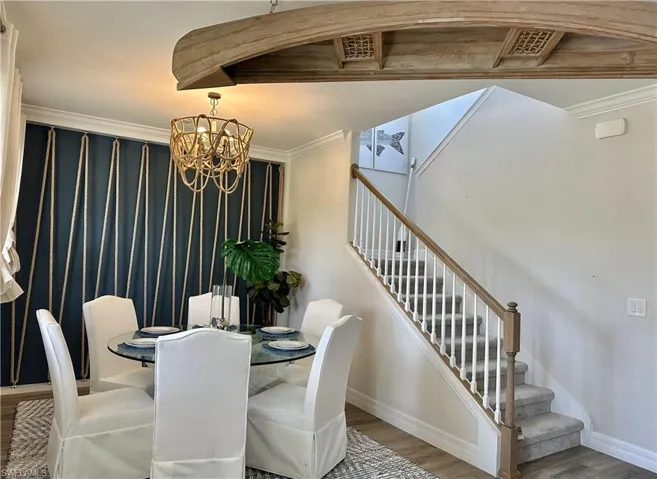 Dining room with ornamental molding, wood finished floors, stairway, and a chandelier