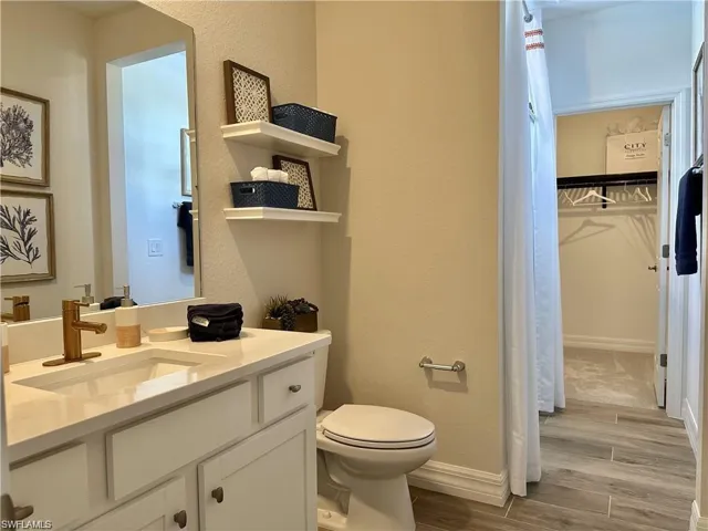 Full bath featuring a textured wall, wood finish floors, vanity, and a spacious closet