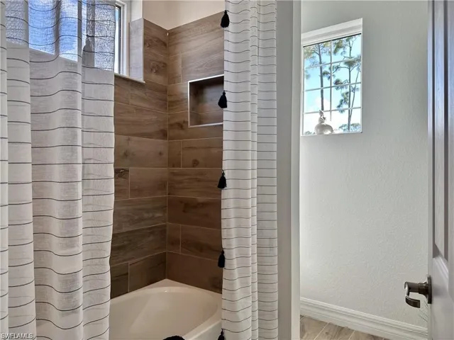 Bathroom with shower / bath combo, healthy amount of natural light, and a textured wall