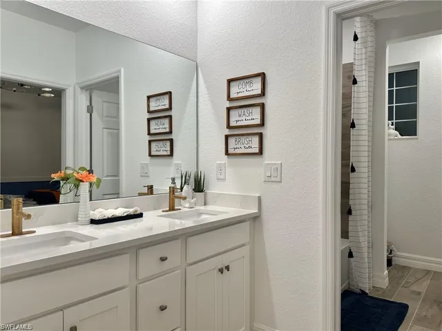 Bathroom with a textured wall, double vanity, wood finish floors, and shower / bath combination with curtain