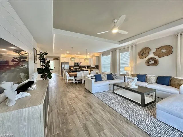 Living room featuring a ceiling fan, light wood-style floors, and a tray ceiling
