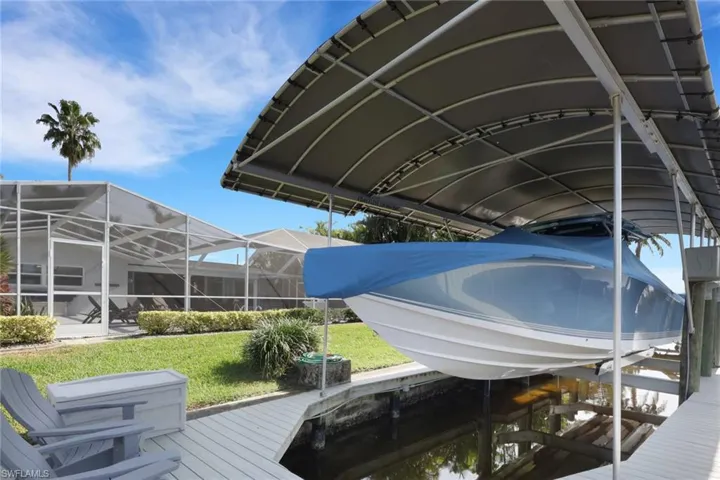 Dock with glass enclosure, boat lift, a sunroom, and a lawn