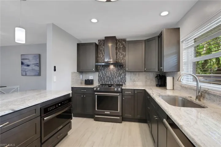 Kitchen featuring decorative light fixtures, light stone countertops, black appliances, wall chimney exhaust hood, and recessed lighting