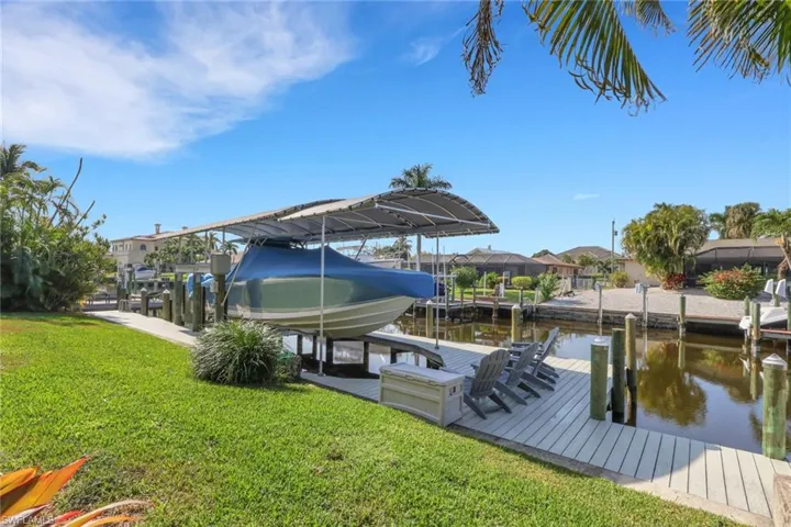 Dock featuring boat lift, a water view, and a yard