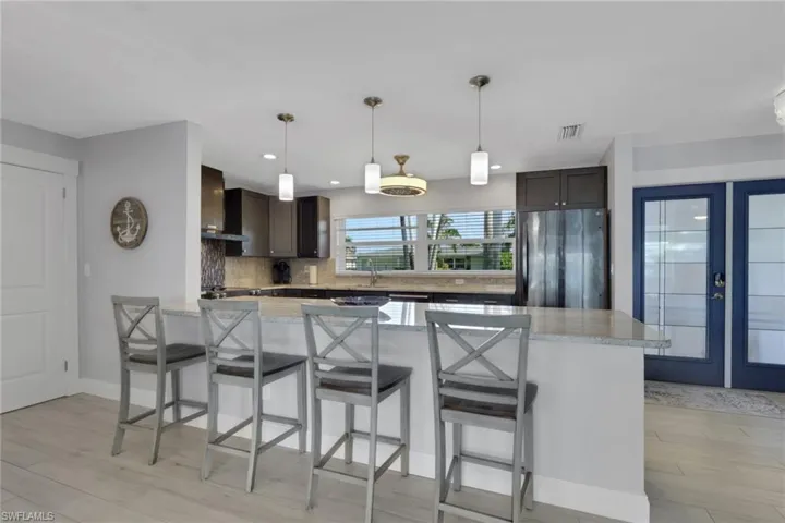Kitchen featuring a kitchen bar, freestanding refrigerator, pendant lighting, dark brown cabinetry, and light stone counters