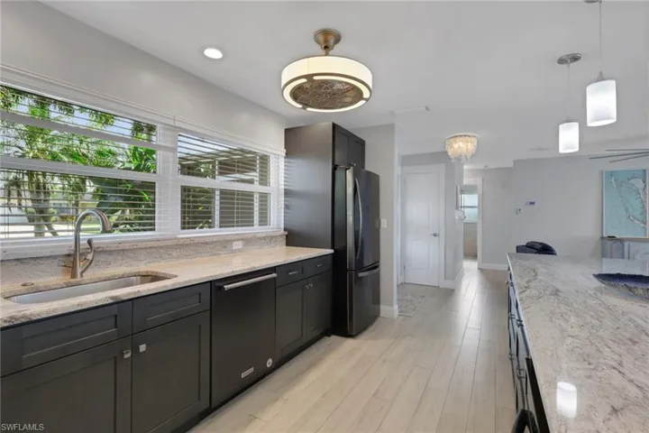 Kitchen with light stone countertops, hanging light fixtures, black dishwasher, and freestanding refrigerator