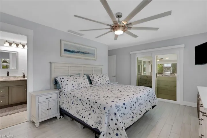 Bedroom featuring ensuite bathroom, light wood-type flooring, ceiling fan, and access to outside